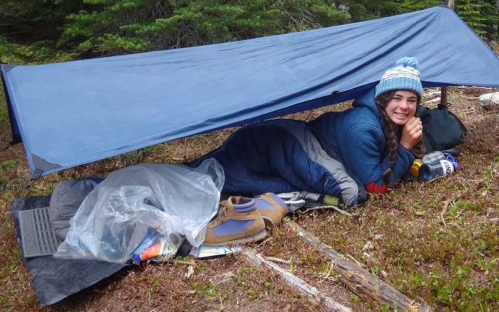 a person smiles while laying under a tarp shelter